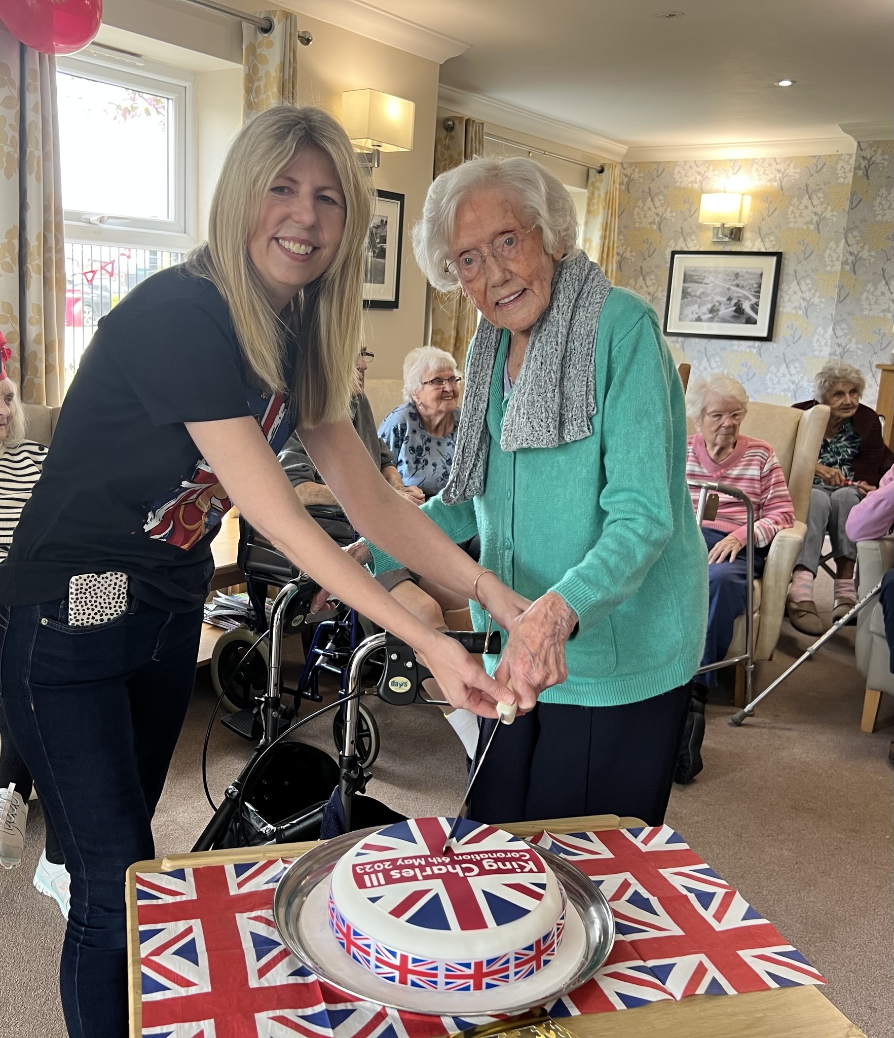 A staff member and a resident cutting the coronation cake,